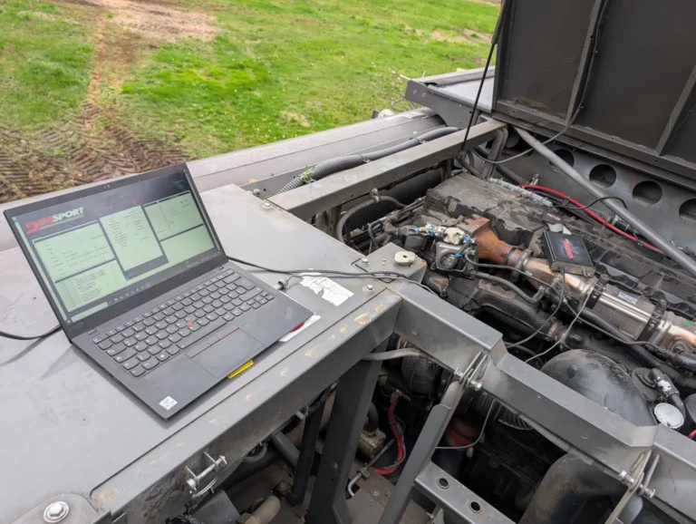Vor-Ort-Service an einer Landmaschine auf dem Feld mit Laptop auf der Motorabdeckung
